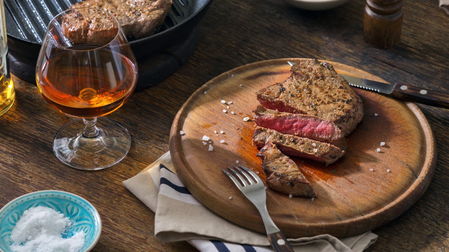 Beef rare grilled steak on wooden board with glass of whiskey